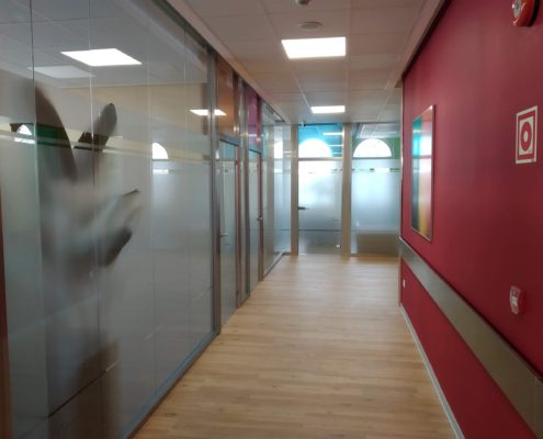Pasillo de oficinas con mamparas y puertas de vidrio.